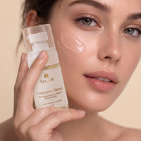 A close-up of a woman holding a bottle of BELADY Tranexamic Serum next to a glossy patch of clear cream on her cheek, set against a warm beige background.